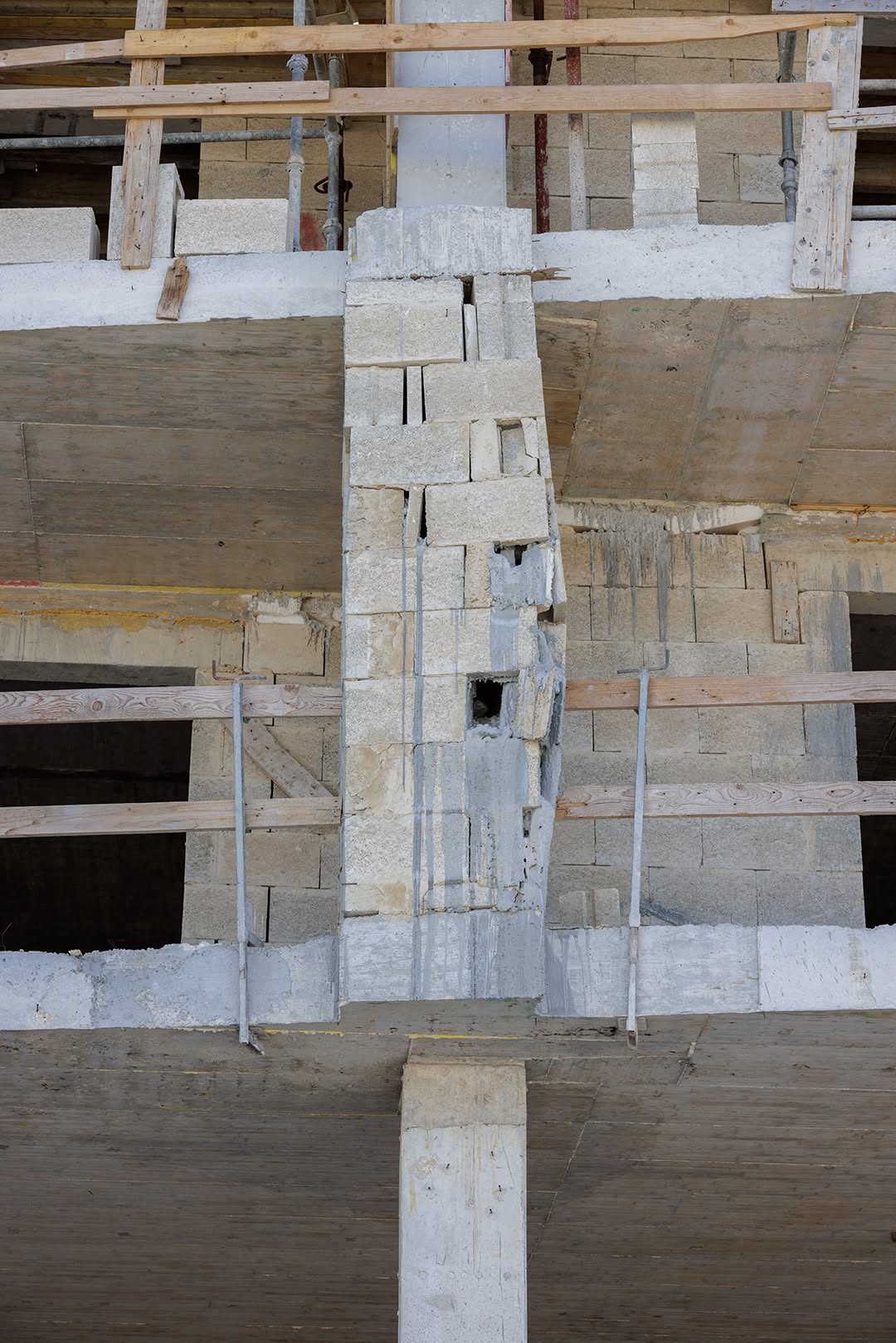 A multi-storey concrete shell under construction, with a central blockwork column leaning out of true, its joints gaping, pieces missing and a hole punched through it.
