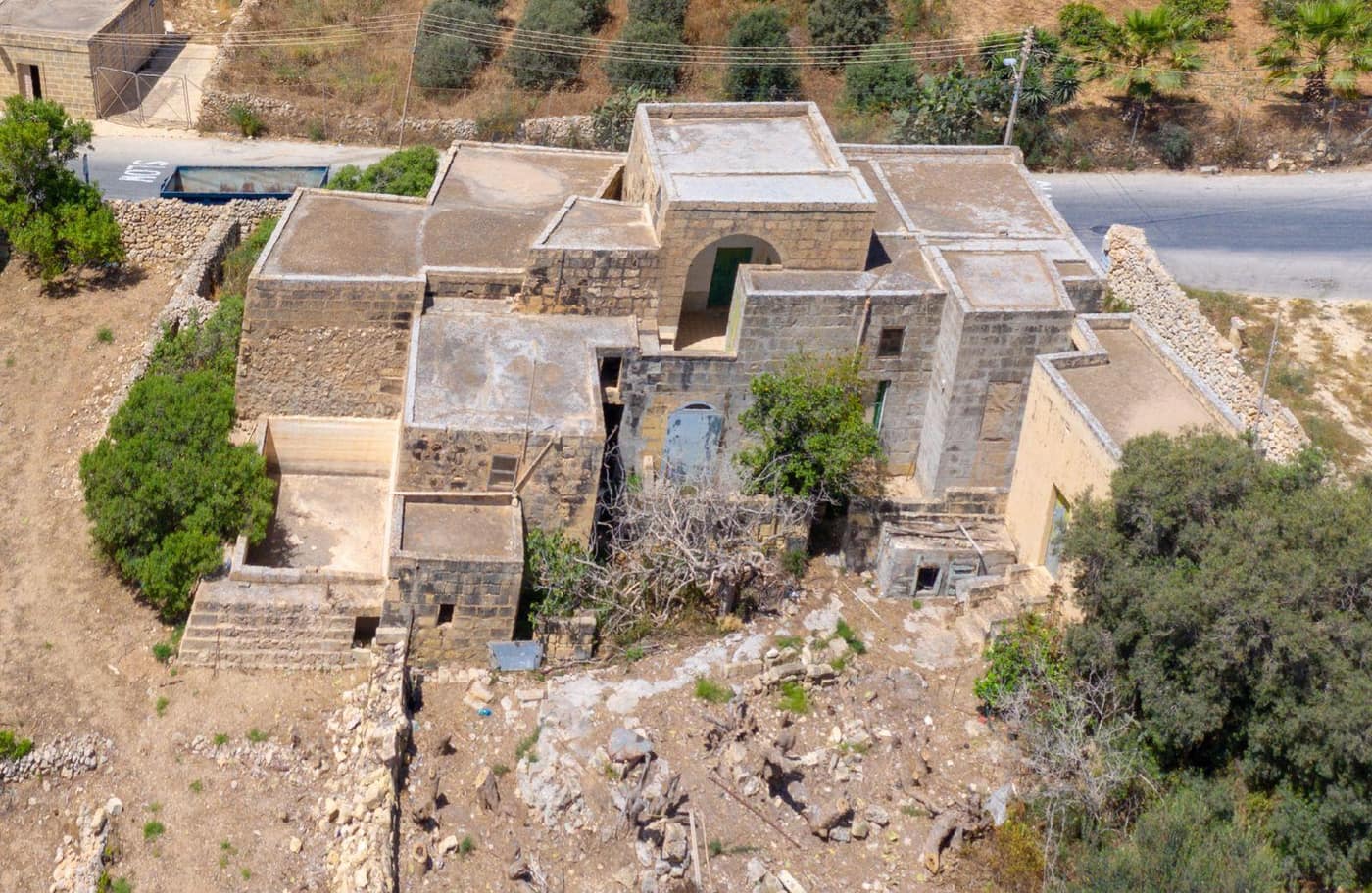 Aerial view of the intact stone farmhouse and its courtyard among fields and trees before demolition