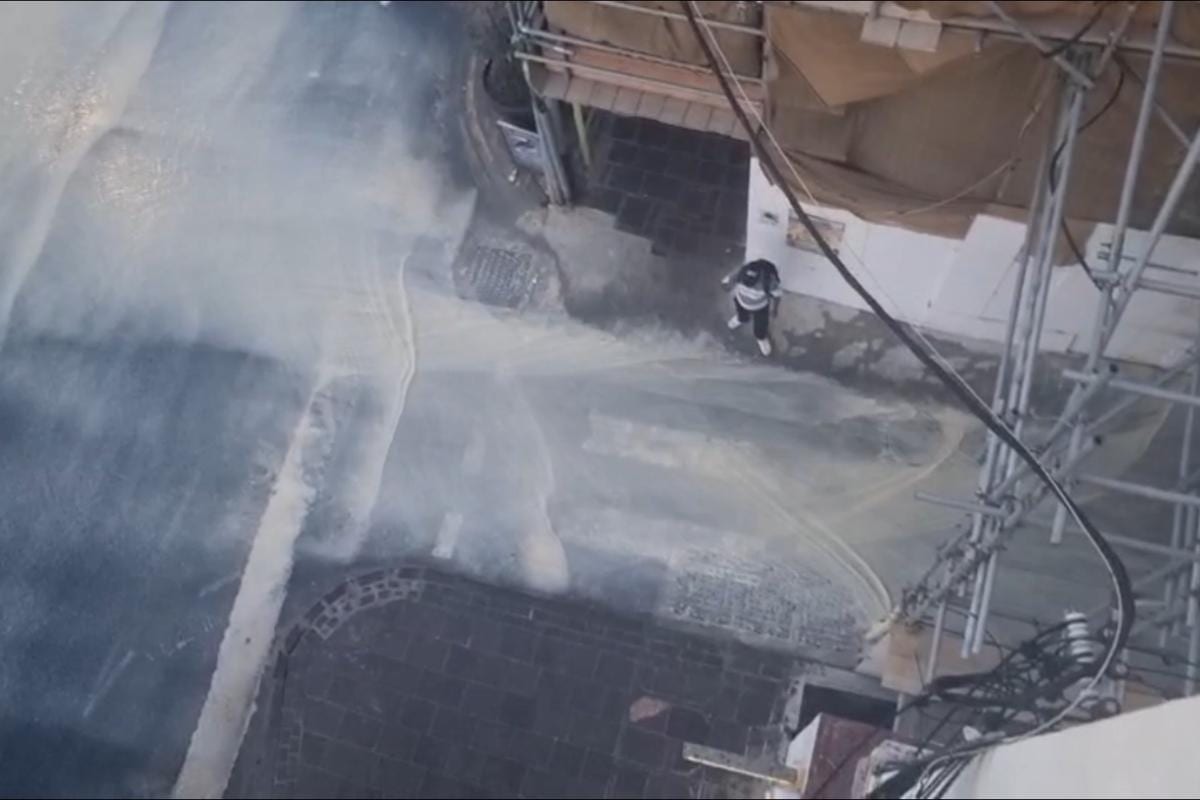 Water streaming down a narrow scaffolded alley, a lone figure standing in the flow