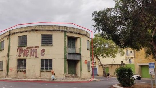 The intact Macaroni Premier pasta factory before demolition: a streamlined interwar industrial building on a curved street corner, its faded painted name still visible, the development plot outlined in red.