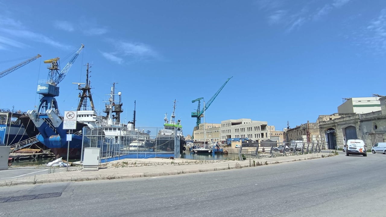The Marsa shipyard, where a barge holding a fenced padel court sits at the quayside among cranes and ships.