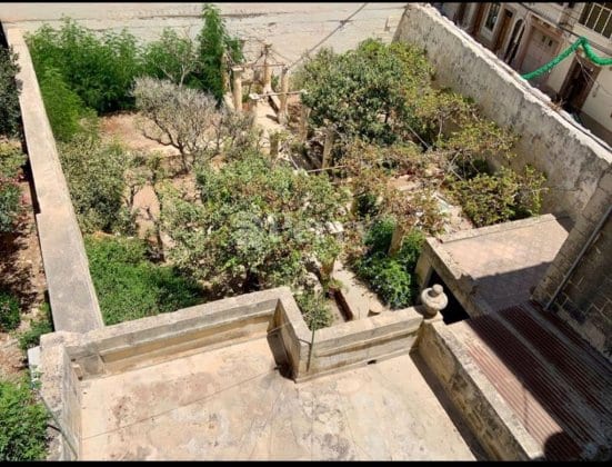 A mature walled garden of trees and shrubs behind Palazzo Torretta, seen from above, with a stone well and terrace.