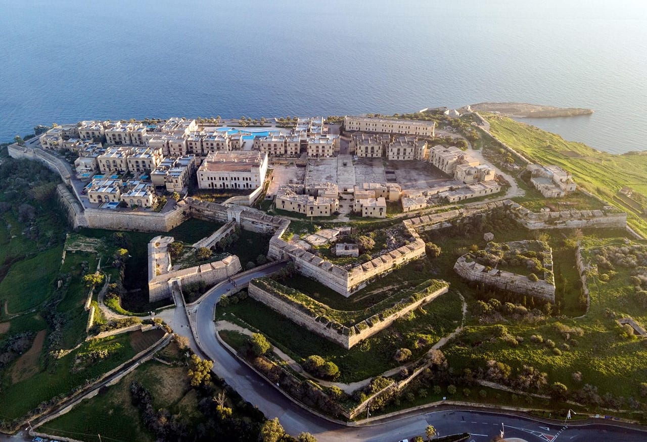 Aerial view of Fort Chambray, Gozo: the star-shaped bastions, the new apartments and pools, and the derelict British barracks on the headland above the sea.