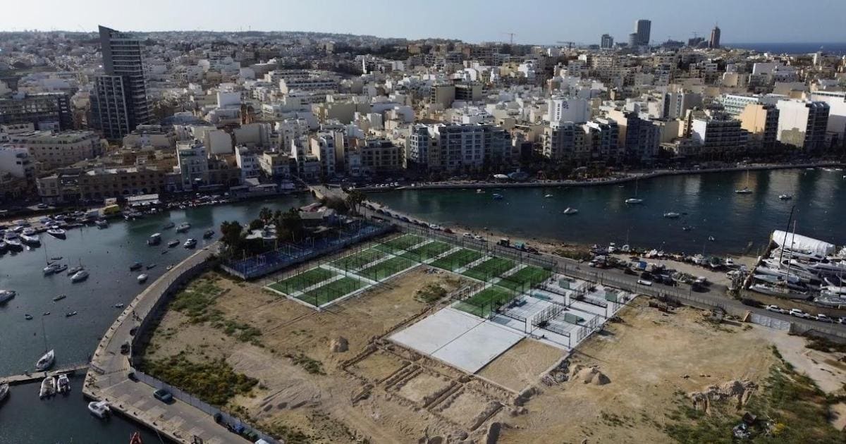 Aerial drone view of rows of glass-walled padel courts built across the former football ground on Manoel Island